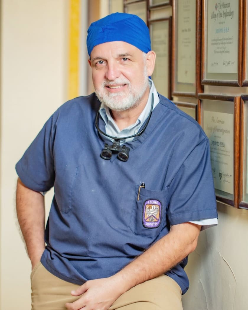 Dr. Jorge Ortiz Díaz frente a su muro de diplomas (formación LSU), especialista en implantes y rehabilitación oral en Saltillo